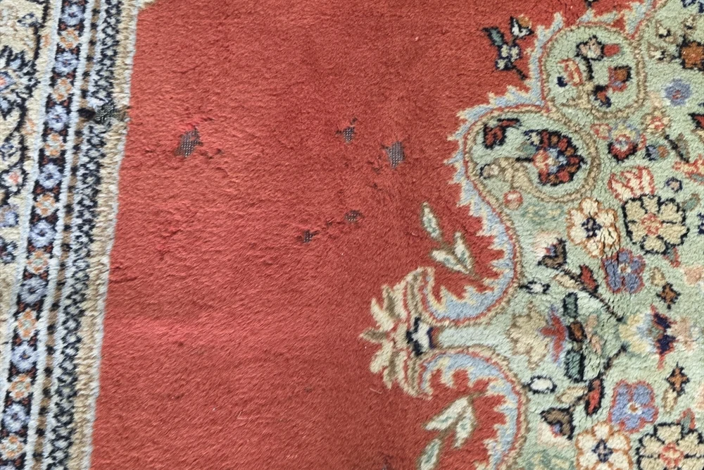Close-up of a red floral rug showing pile texture and small areas where the underlying weave is visible.